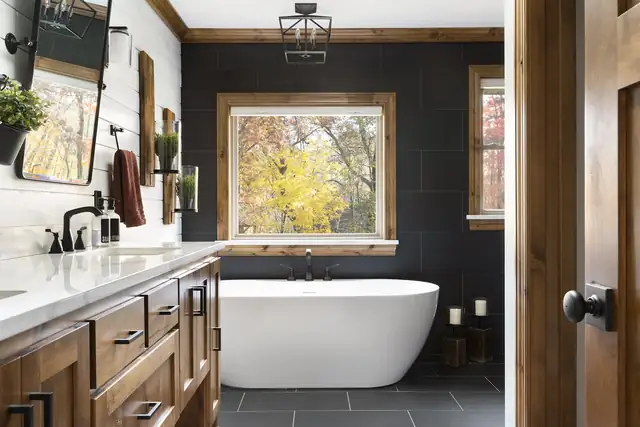 Bathroom with a freestanding soaking tub, black tile accent wall, window and rich wood vanity