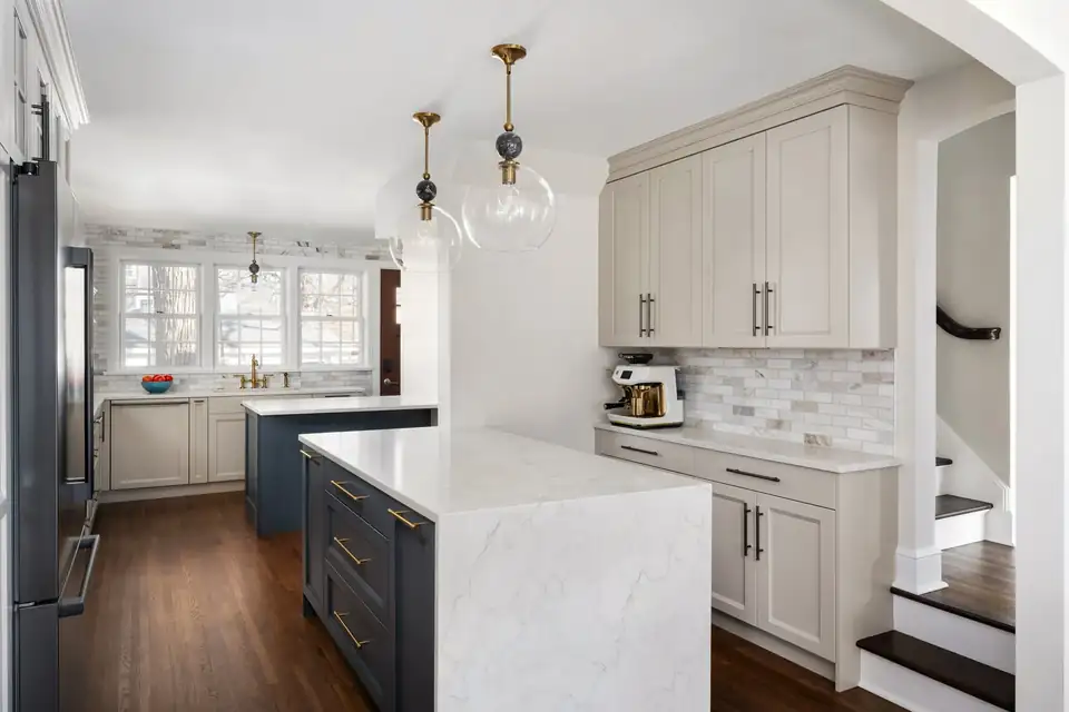 Kitchen remodeling in St. Paul: St. Clair kitchen with greige Shaker cabinets, a white waterfall quartz island, gray tile backsplash and glass pendants