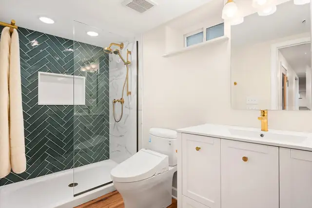 Emerald and Gold bath with green herringbone shower tile, brass fixtures and a white vanity