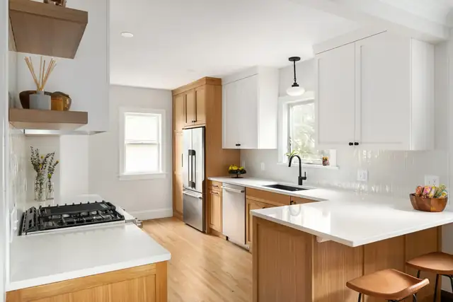 Kitchen by Wise Design & Remodel with white upper cabinets, wood base cabinets, a white quartz peninsula and floating wood shelves