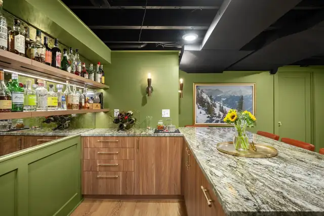 Basement bar with olive green cabinets, wood drawer fronts, a granite counter and open bottle shelving