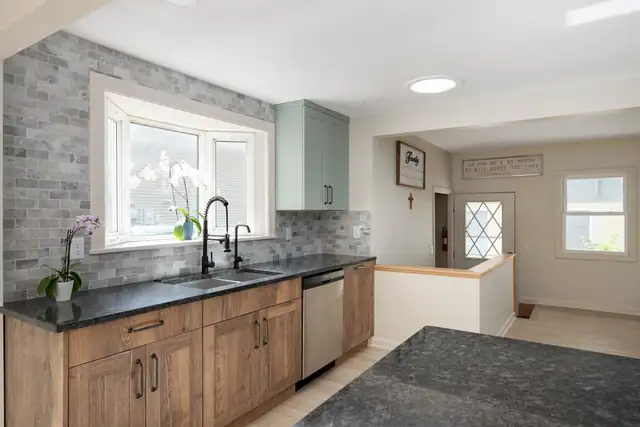 Tobacco and Sage kitchen with warm wood base cabinets, sage green uppers and a gray stone backsplash