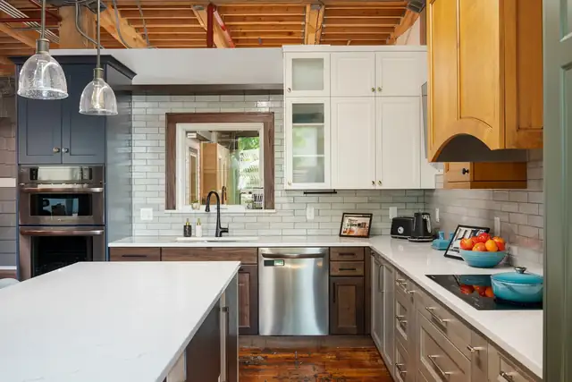 Kitchen display at the Wise Design & Remodel showroom in St. Paul with wood and white cabinets, a quartz island and glass pendants